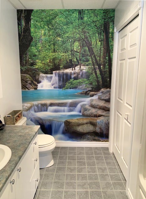 Erawan Waterfalls Wall Mural, as seen on the wall of this powder room, is a photo wallpaper of turquoise water spilling over rocks in a lush Thailand forest from About Murals.