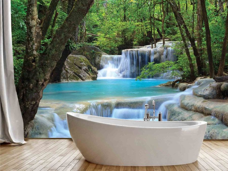 Erawan Waterfalls Wall Mural, as seen on the wall of this peaceful bathroom, is a photo wallpaper of turquoise water gushing over large rocks in a green forest from About Murals.