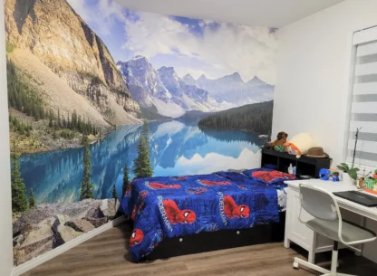 Moraine Lake Wallpaper, as seen on the wall of this kids room, is a photo mural of mountains surrounded by a pine tree forest and glacier lake from About Murals.