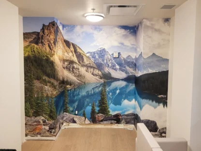 Moraine Lake Wallpaper, as seen on the wall of this room, is a photo wall mural of Canadian mountains towering over a blue lake in summer from About Murals.