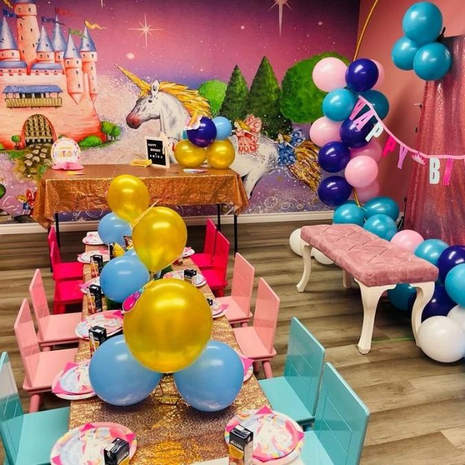 Princess Castle Wallpaper, as seen on the wall of this children’s party room, is a purple kids mural with a pink castle and white unicorn from About Murals.