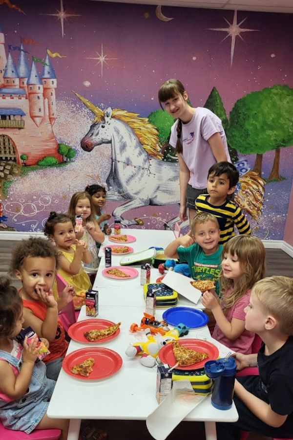 Princess Castle Wallpaper, as seen on the wall of this party place, is a kids mural with a pink castle and white unicorn on a purple background from About Murals.