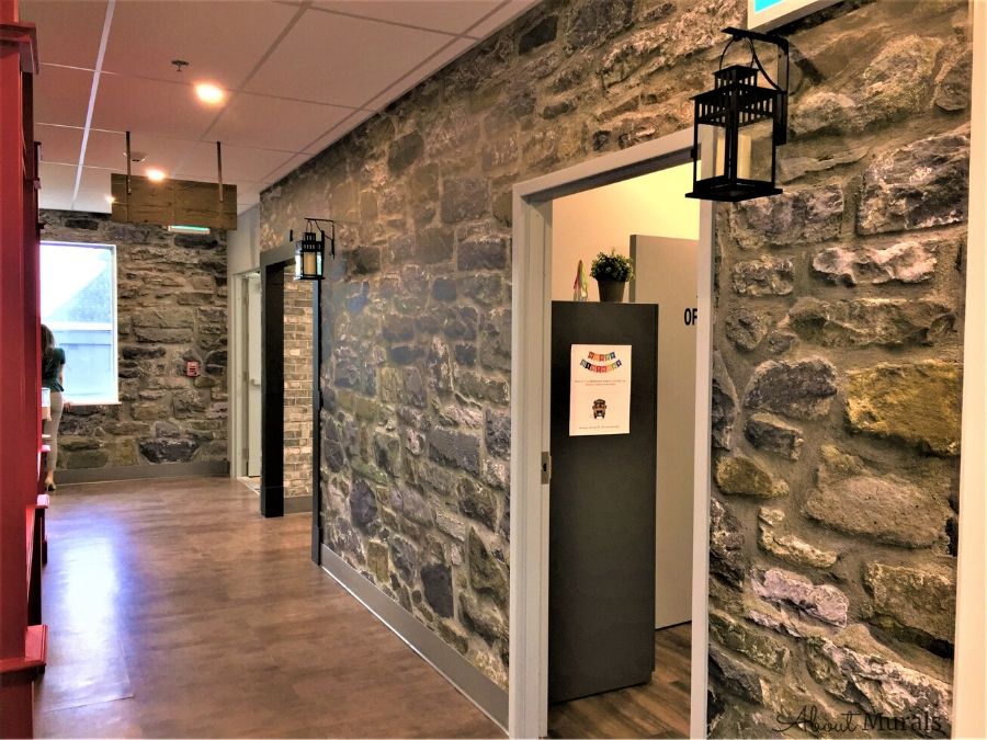 Stone Wall Mural, as seen in this hallway, features grey stacked stones with hints of blue, purple and yellow. Stone wallpaper sold by AboutMurals.ca.