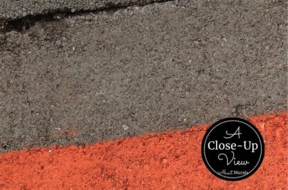 A close-up view of an orange painted stripe on grey cement from a concrete wallpaper sold by About Murals.