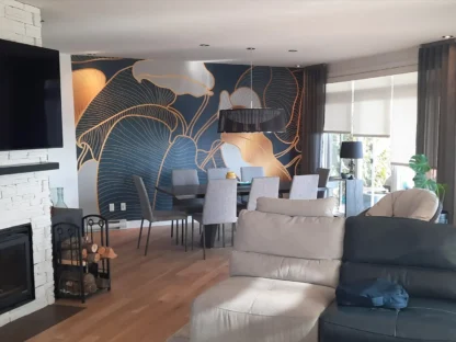 Philodendron Wallpaper, as seen on the wall of this family room behind a fireplace, is a tropical leaf wall mural with blue, gold and gray leaves from About Murals.
