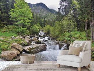Forest River Wallpaper, as seen on the wall of this living room, is a photo mural of a mountain towering over a green pine forest and stream running over rocks from About Murals.