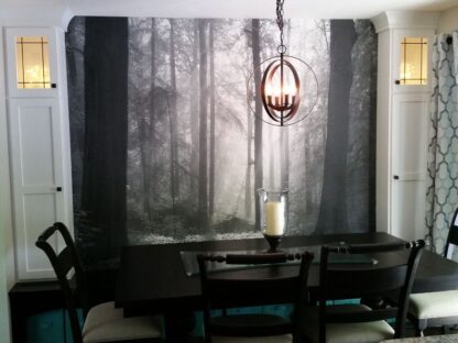 Black and White Woods Wallpaper, as seen on the wall of this dining room, is a photo wall mural of sunbeams shining through gray trees in a foggy forest from About Murals.
