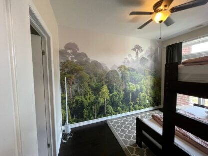 Misty Rainforest Wallpaper, as seen on the wall of this bedroom, is a wall mural of a foggy clouds setting over green trees in a tropical jungle from About Murals.