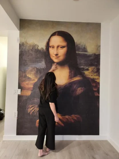 Mona Lisa Wallpaper, as seen on the wall of a room with a customer feeling her face, is a mural of the famous painting from About Murals