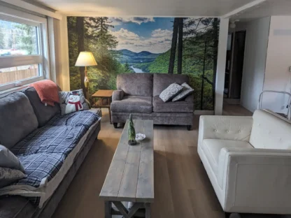 Mountain River Wallpaper, as seen on the wall of this sitting room, is a wall mural of a nature scene through a forest from About Murals