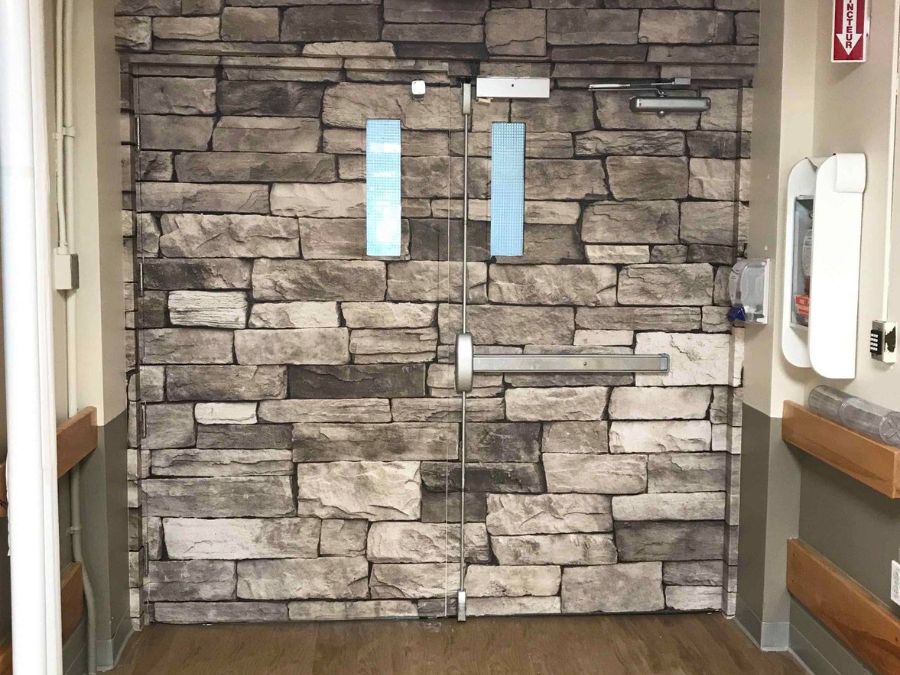 A door wrap in a dementia unit camouflages the door to look like a stone wall, acting as an exit diversion so residents don't wander or escape.