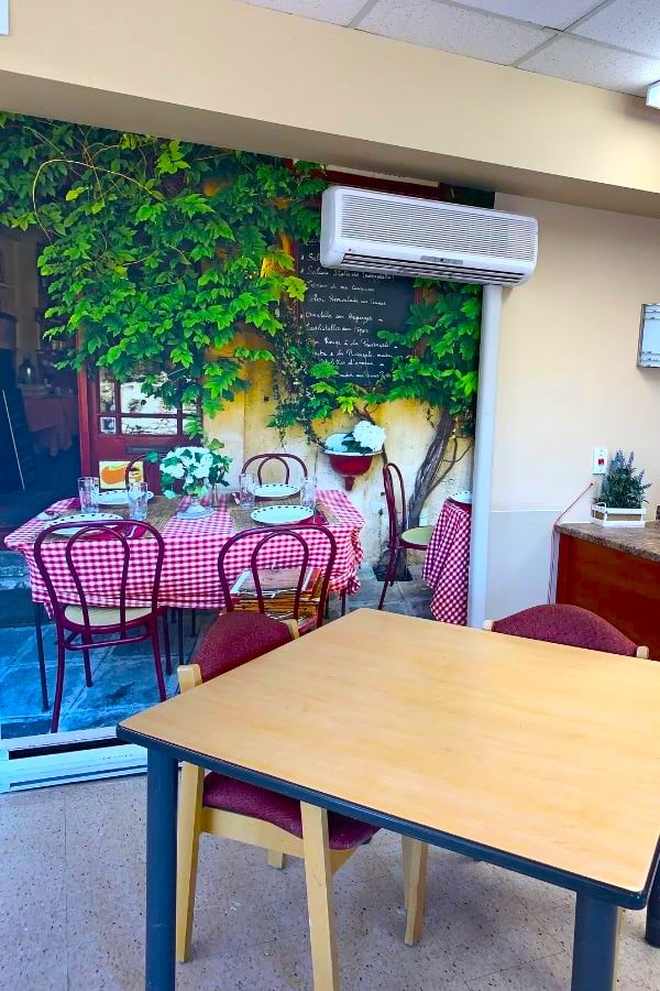 Murals for memory care, like this cafe wallpaper in a senior living dining room featuring an outdoor bistro with red checker table, can help stimulate resident's appetite.
