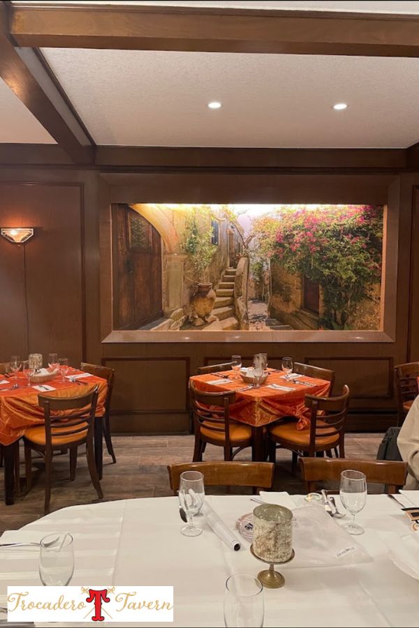 Italian restaurant mural, featuring a cobblestone village in Sicily, on a wall behind set tables at an Italian restaurant in Hamilton, ON, Canada by About Murals.