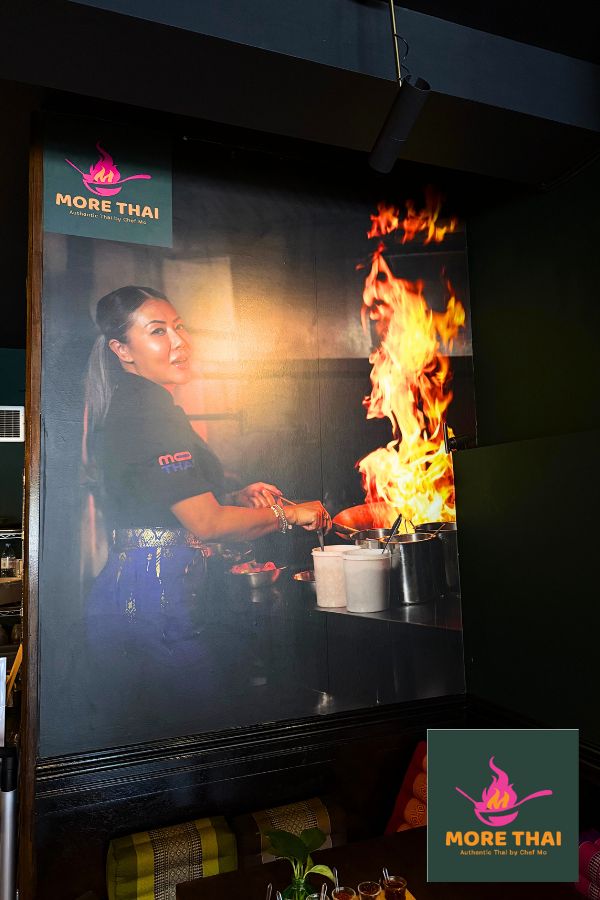 Restaurant wall mural created from a high resolution photo of a restaurant owner cooking over a flame and the More Thai restaurant logo in the top left corner by About Murals.
