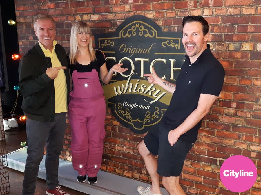 A selfie wall for restaurant, featuring a logo for a whiskey lounge over a red brick wall, with two interior designers and one wallpaper installer in front.
