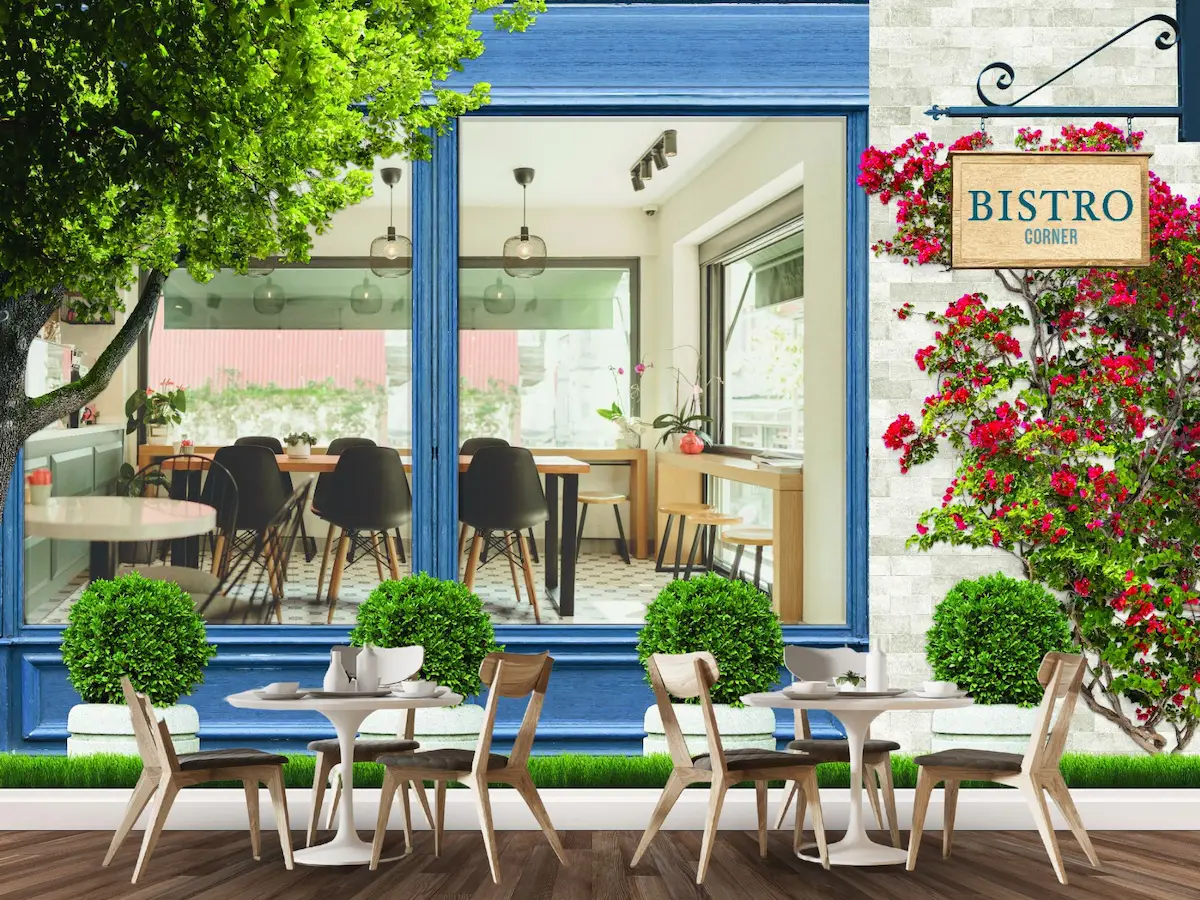 Blue Bistro Wallpaper, as seen on the wall of a restaurant, is a mural featuring an exterior view of a cafe window surrounded by plants and flowers, looking inside the bistro with tables and chairs from About Murals Canada.