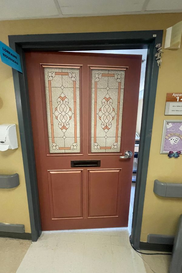 Dementia Door Wallpaper, as seen in this memory care corridor, is a brown door wrap that helps residents find their room from About Murals