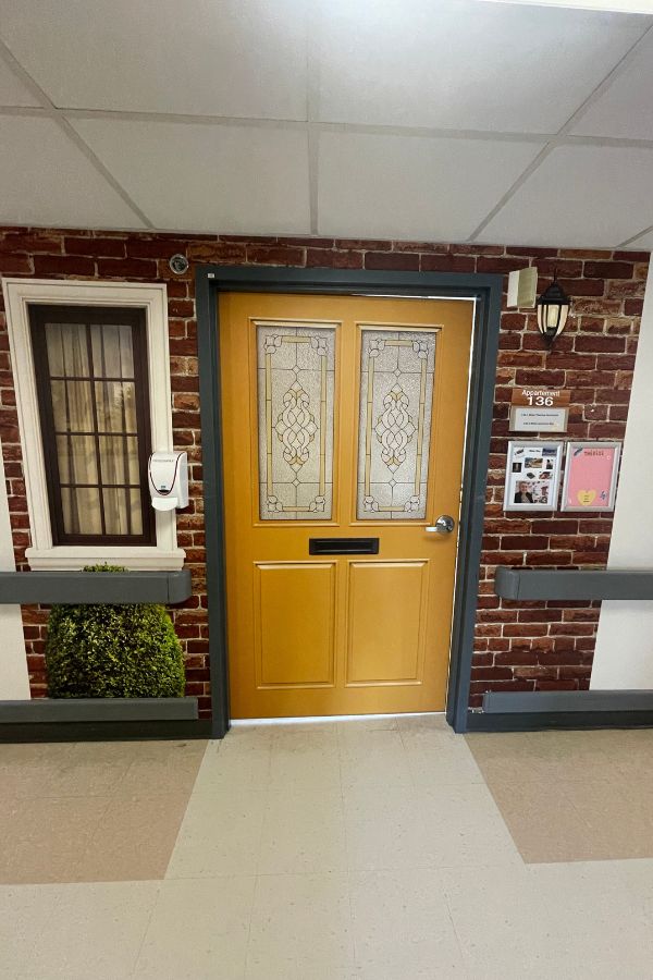 Dementia Door Wallpaper, as seen in this memory care unit, is a yellow door decal to help residents find their bedroom from About Murals